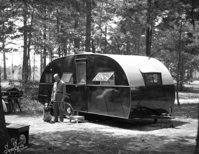 Travel trailer with man and dog standing in front, located in the woods