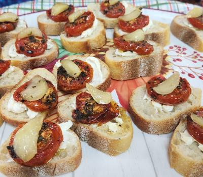 bread topped with candied garlic, thyme, and roasted tomatoes on a paper plate