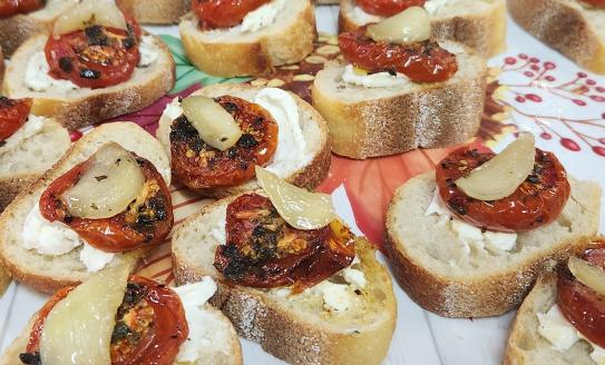 bread topped with candied garlic, thyme, and roasted tomatoes on a paper plate